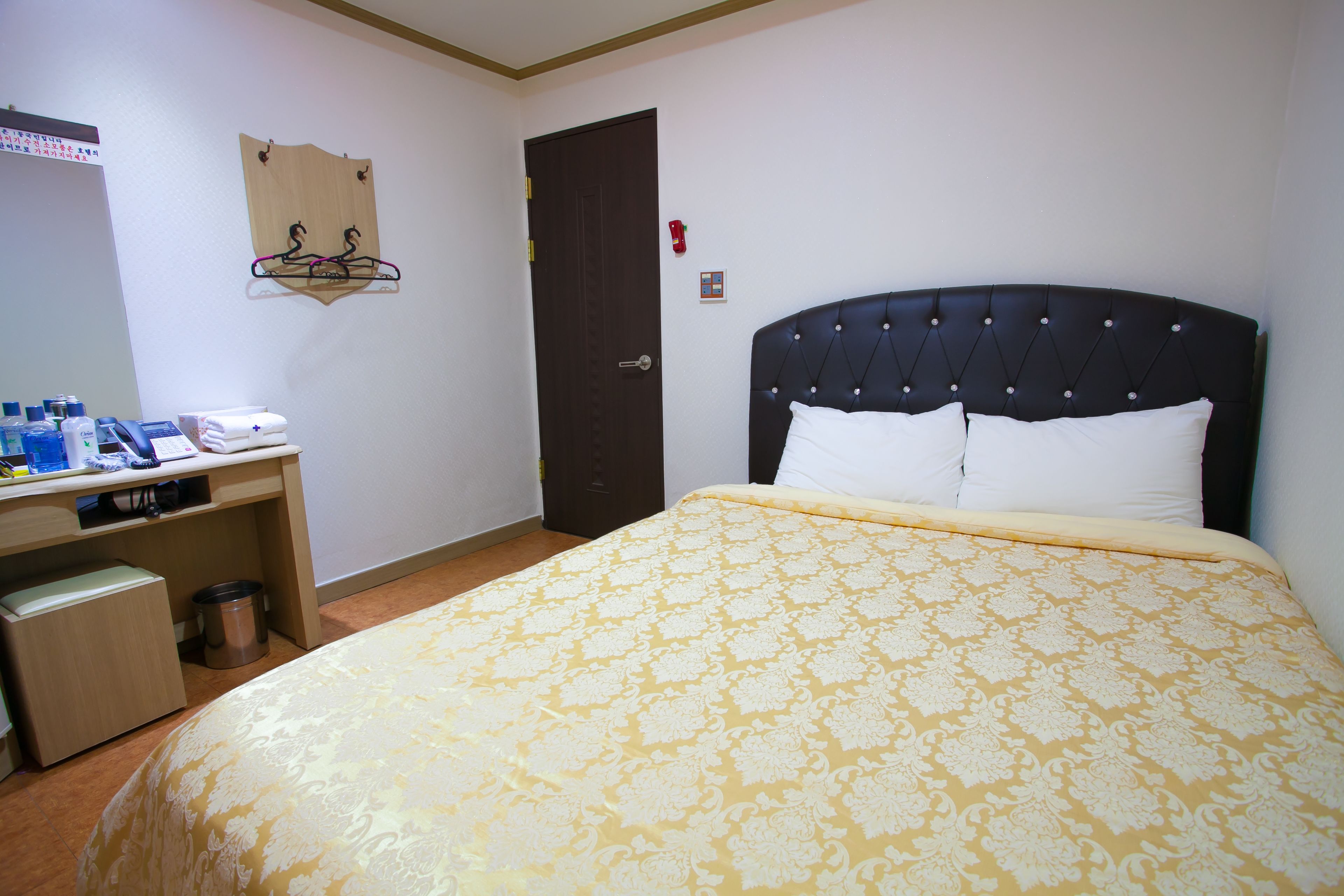 A hotel room with a bed, a desk with toiletries, a coat rack, and a door.