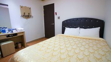 A hotel room with a bed, a desk with toiletries, a coat rack, and a door.