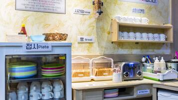 A kitchen area with labeled storage for bread, cereal, and soup. There are also plates, cups, and a toaster on the counter.