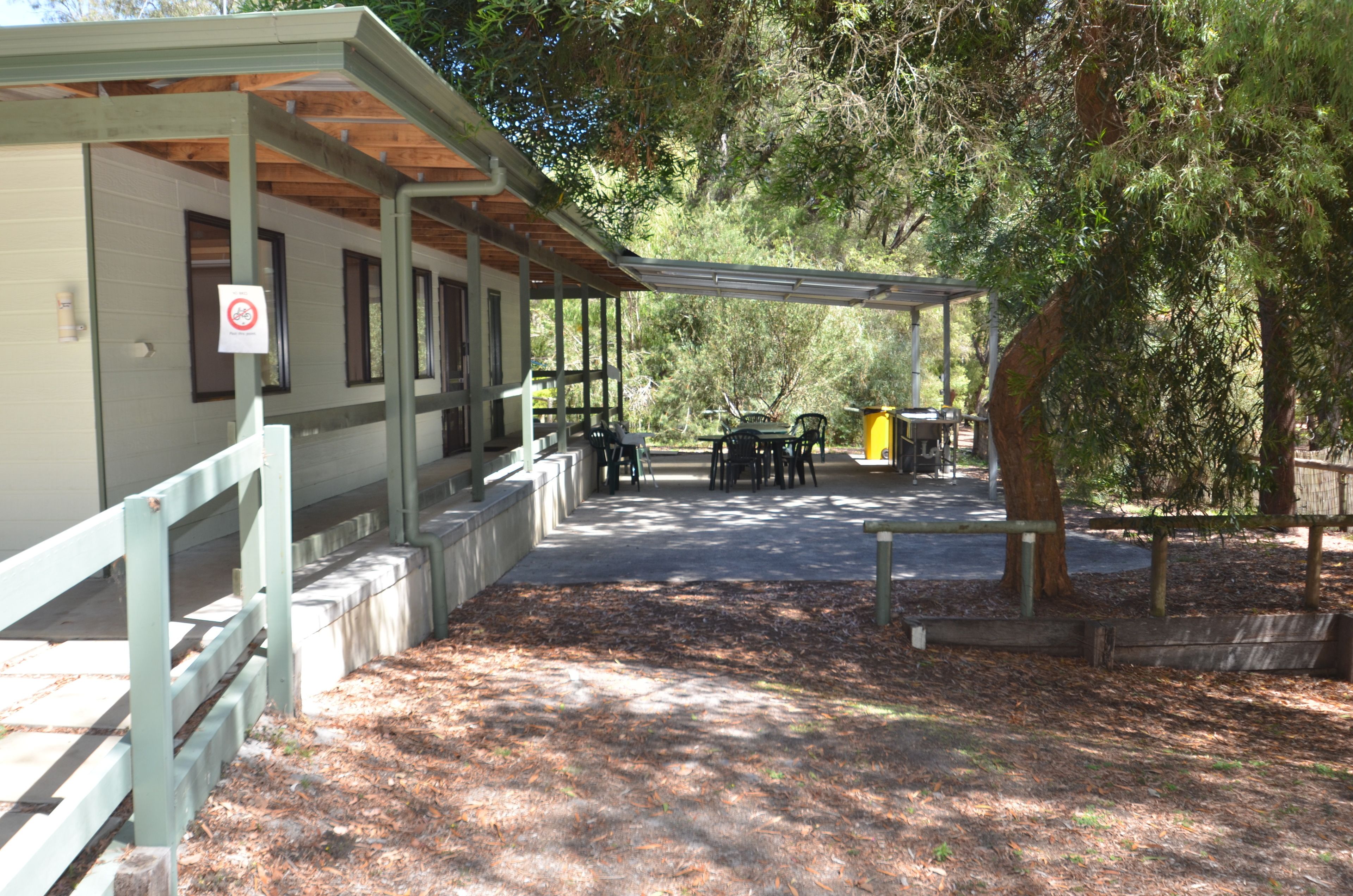 A covered outdoor seating area with tables and chairs, a wooden fence, and a building with windows.