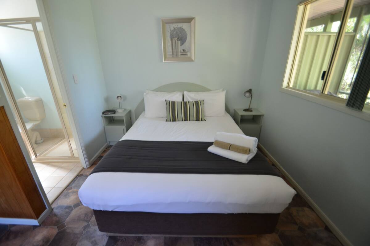 A neatly made bed with white and striped pillows, a dark headboard, and a small bedside table with a lamp.