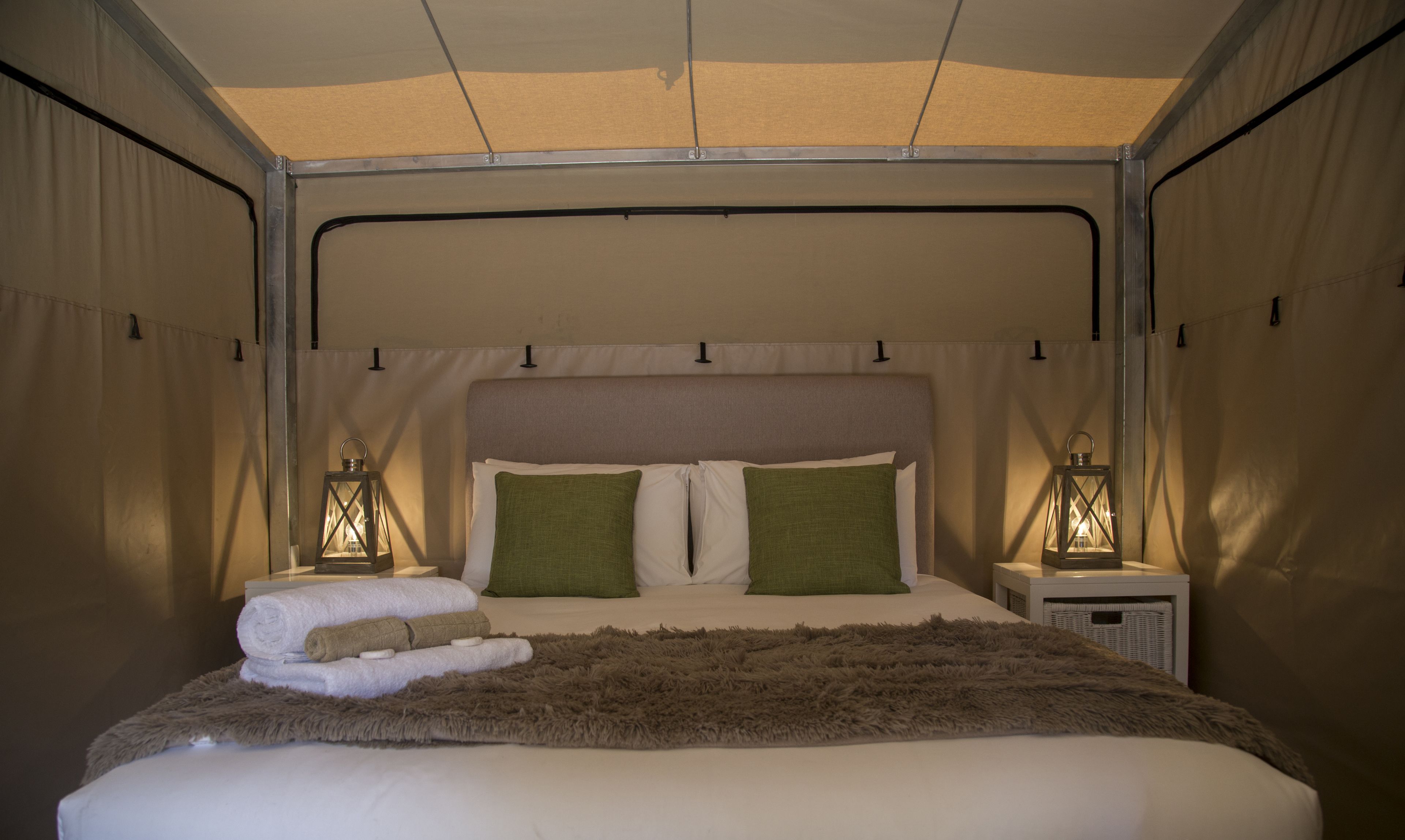 Una habitación tipo tienda con una cama, dos almohadas verdes, un tapete marrón mullido y dos faroles.