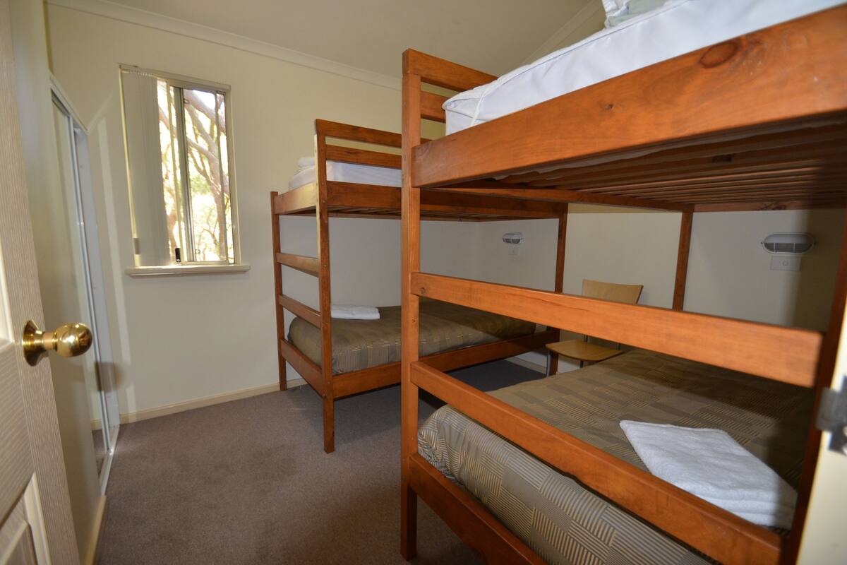 A room with three bunk beds, a window, and a door with a brass doorknob.
