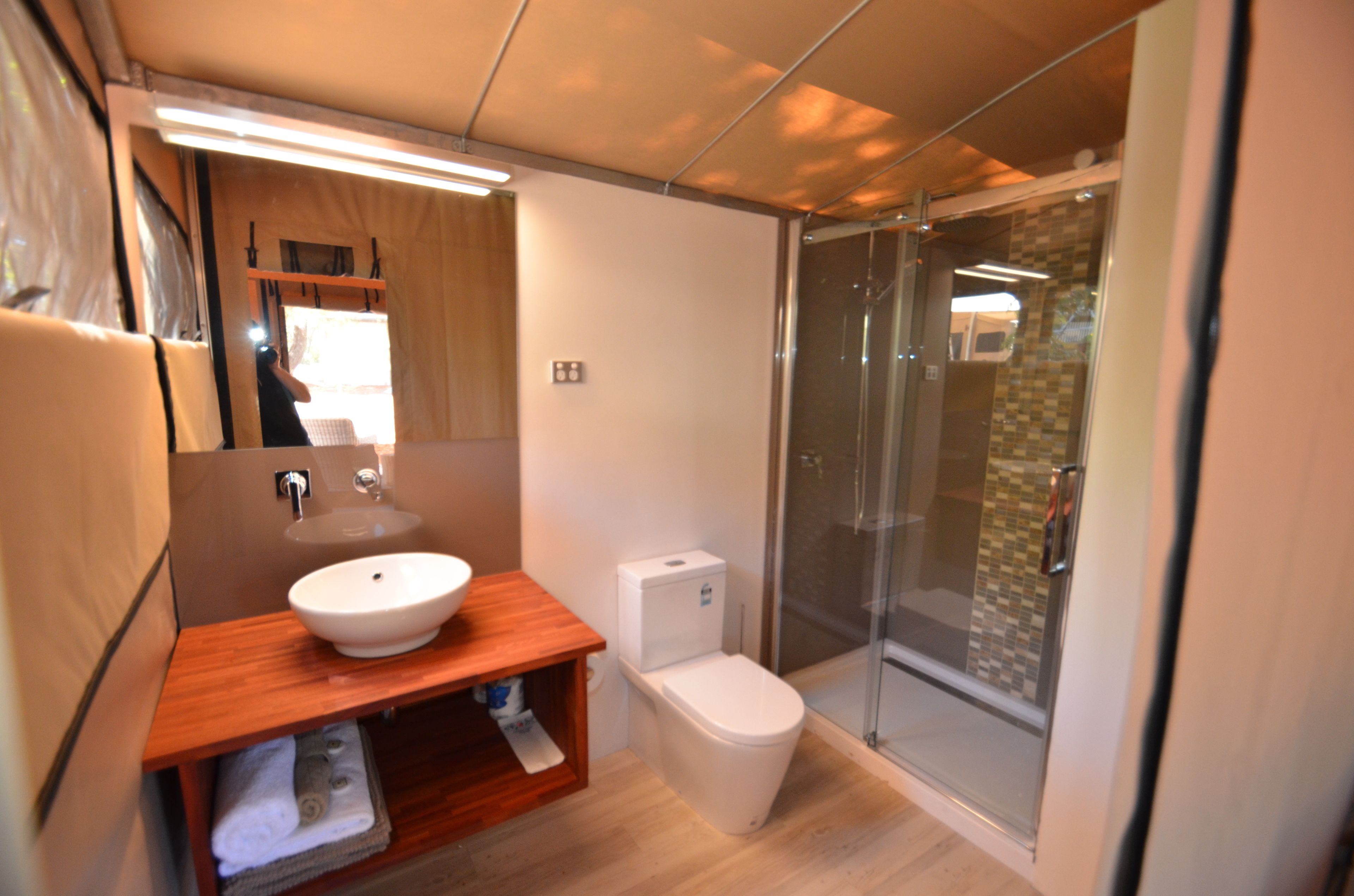 A modern bathroom with a wooden vanity, a white sink, a toilet, and a glass shower enclosure.