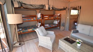 Una habitación con carpas, camas literas, un sofá, una silla y una mesa con una lámpara y una planta pequeña.