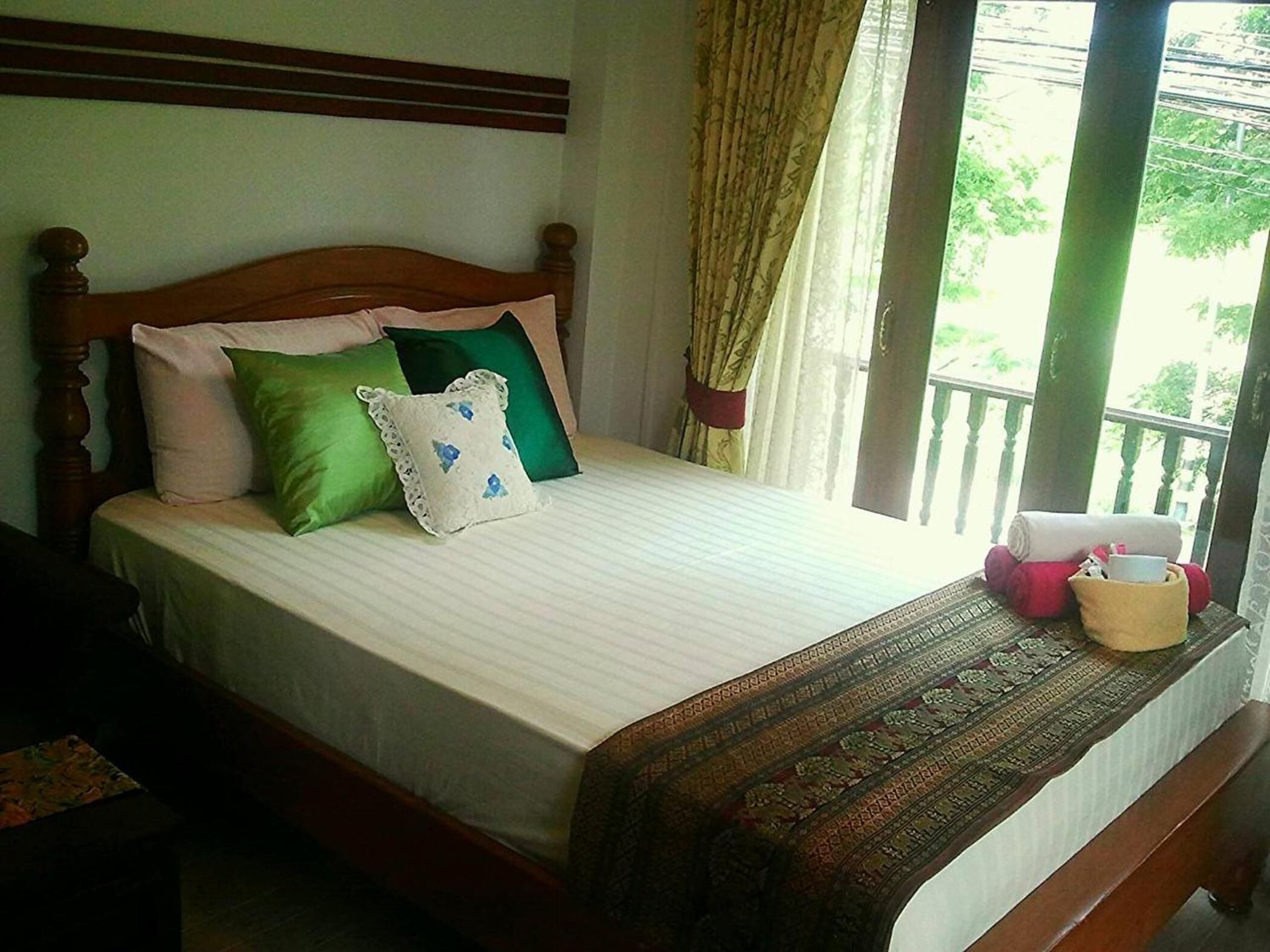 A bed with a wooden headboard, green and white pillows, a patterned bedspread, and a window with curtains.