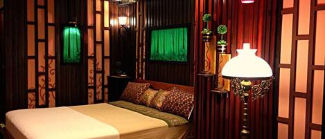 A neatly made bed with a wooden frame, a bedside lamp, and a green curtain.