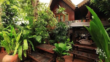 A wooden outdoor seating area with benches and tables, surrounded by lush greenery and potted plants.