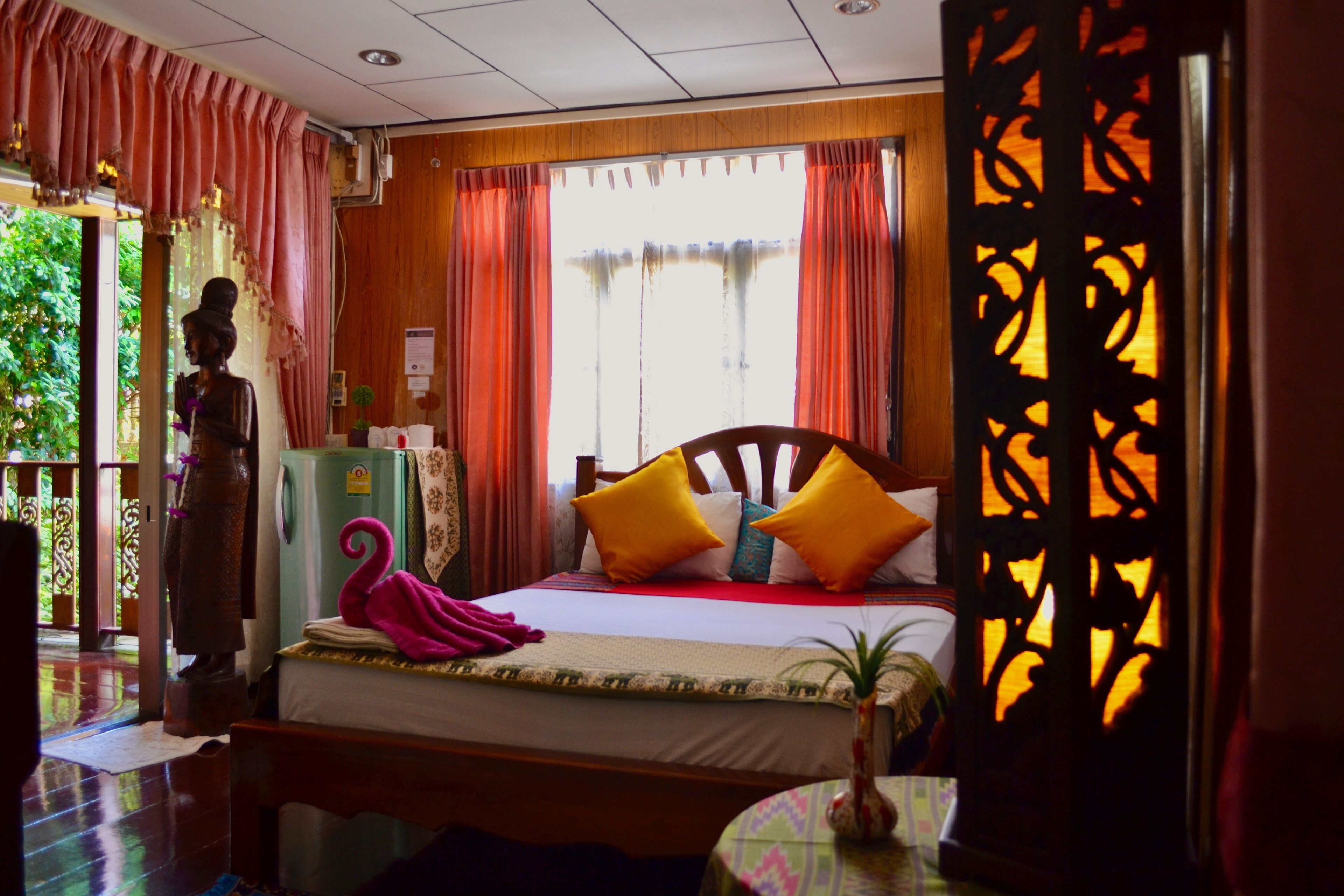 Una habitación con cama, una estatua, una ventana con cortinas y un biombo decorativo.