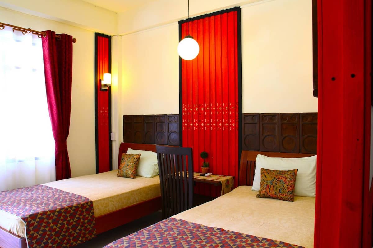 Une chambre d’hôtel avec deux lits simples, une petite table, une chaise et un rideau rouge.
