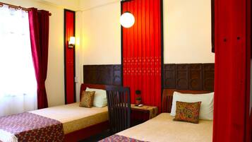 A hotel room with two single beds, a small table, a chair, and a red curtain.