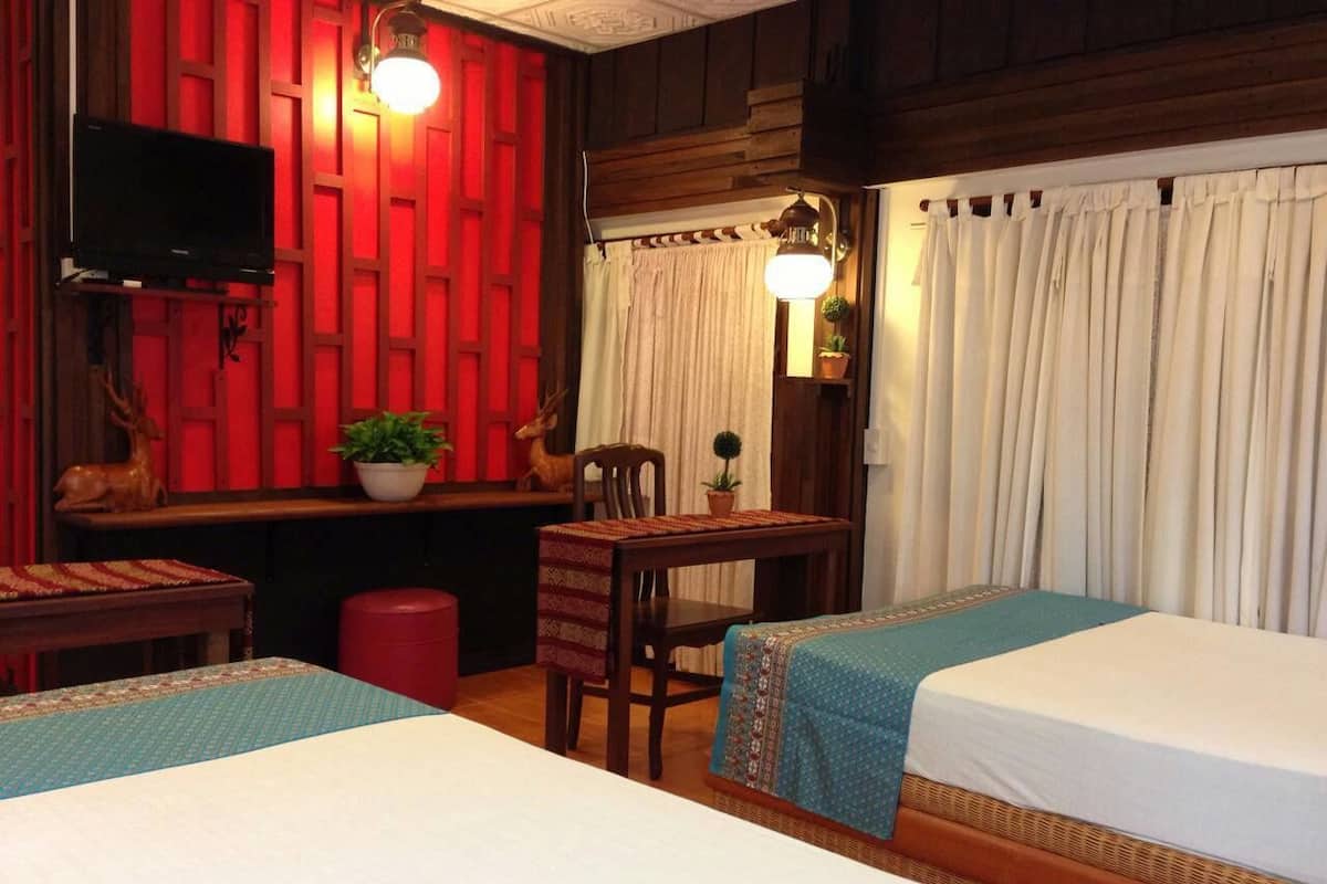 Une chambre d’hôtel avec deux lits, un bureau avec une chaise, une télévision et un mur rouge.