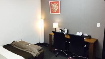 A hotel room with a bed, a desk with a chair, a lamp, a picture on the wall, and a calendar on the desk.