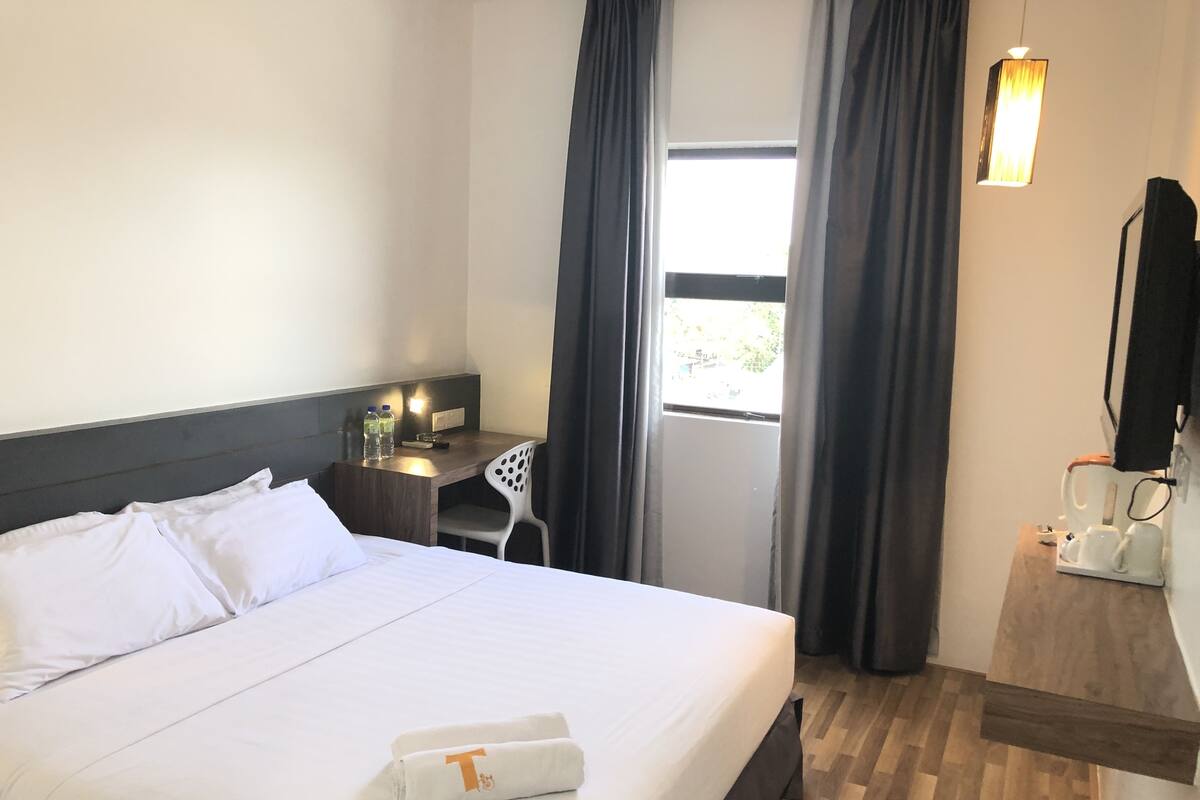 Une chambre d’hôtel avec un grand lit, un bureau avec une chaise, une fenêtre avec des rideaux et une petite table sur laquelle se trouve une machine à café.