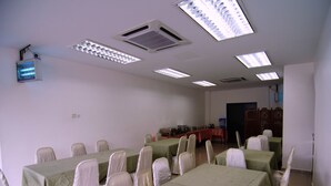 Un salón de conferencias con mesas y sillas, conductos de aire acondicionado y una televisión en la pared.