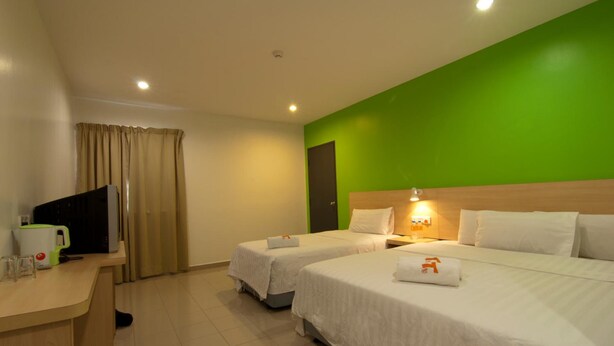 Una habitación de hotel con dos camas, un escritorio con cafetera y una pared de acento verde.