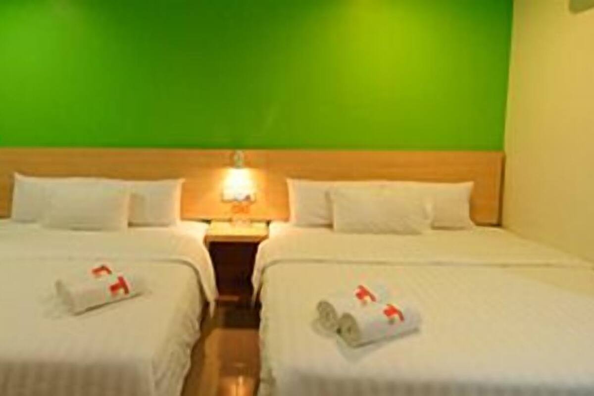 Une chambre d’hôtel avec deux lits, une tête de lit en bois et un mur vert.