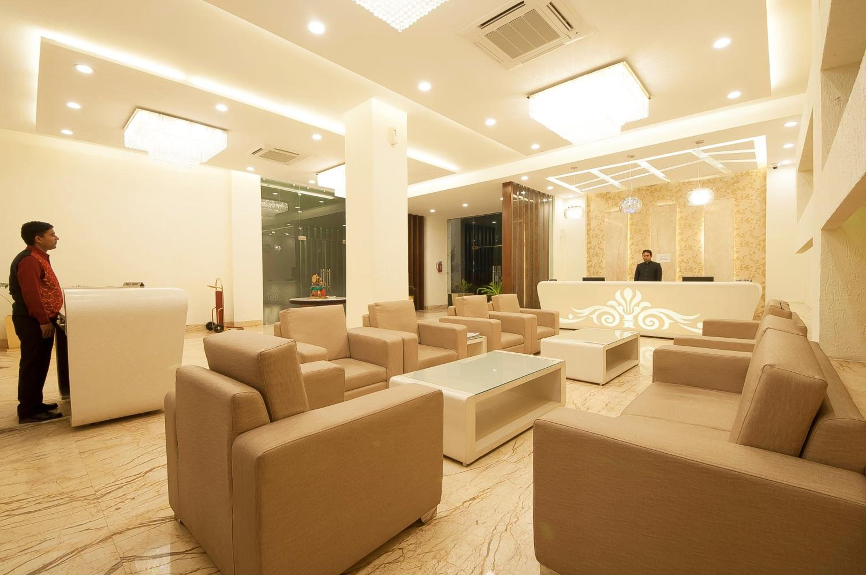 A modern hotel lobby with beige sofas, a reception desk, and a marble floor.