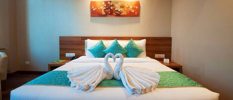 A hotel room with a neatly made bed, a painting on the wall, and a nightstand with a phone and a sign.