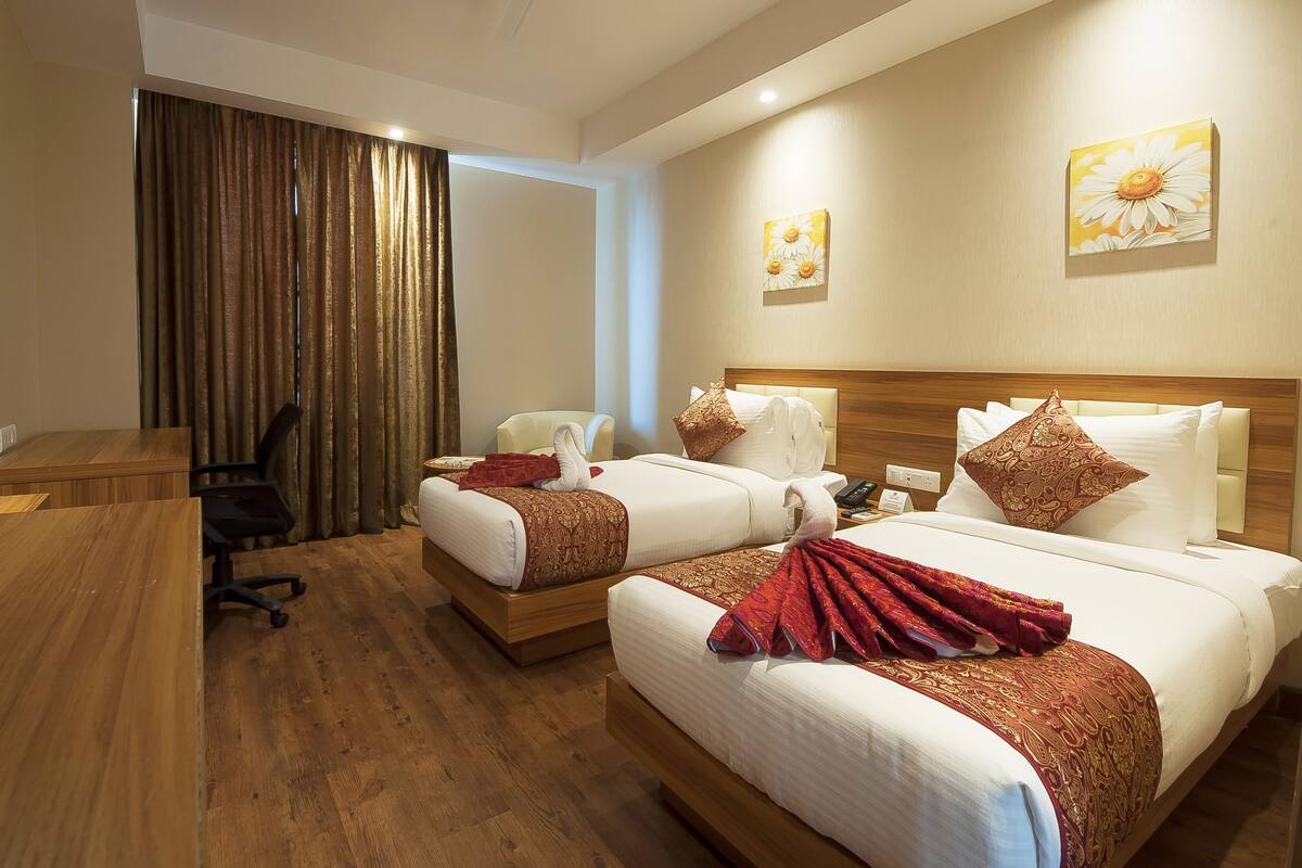 A hotel room with two beds, a desk, a chair, and a television.