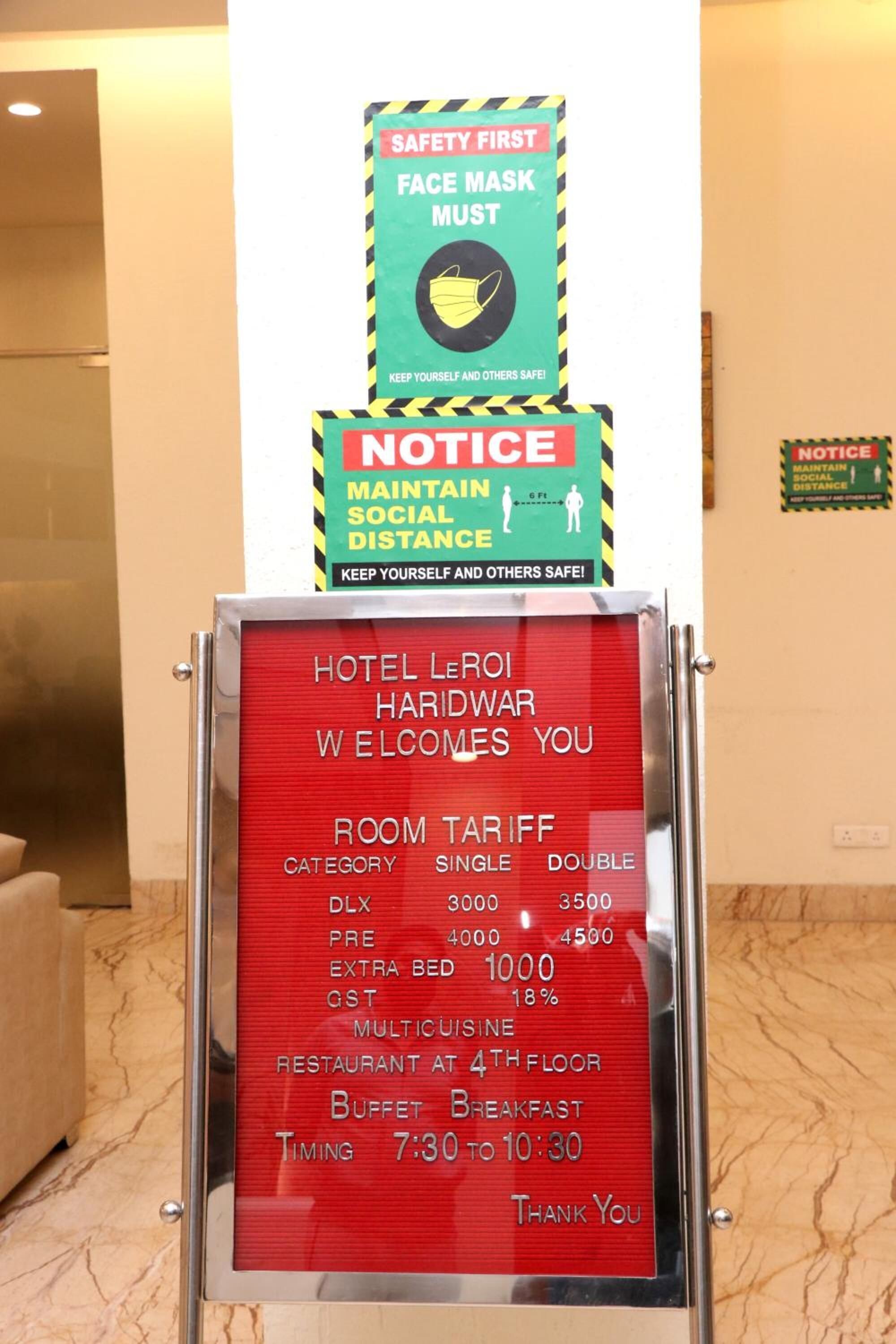 Ein Willkommensschild des Hotels mit Zimmerpreisen, einer Hinweistafel zur Einhaltung des sozialen Distanzes und einer Maskenpflicht zum Schutz der Gesundheit.