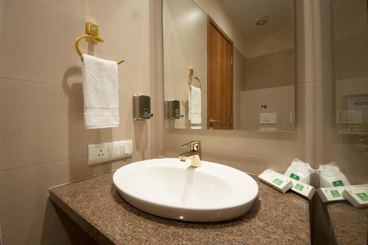 A bathroom with a round white sink, two towel racks, a mirror, and toiletries on the counter.