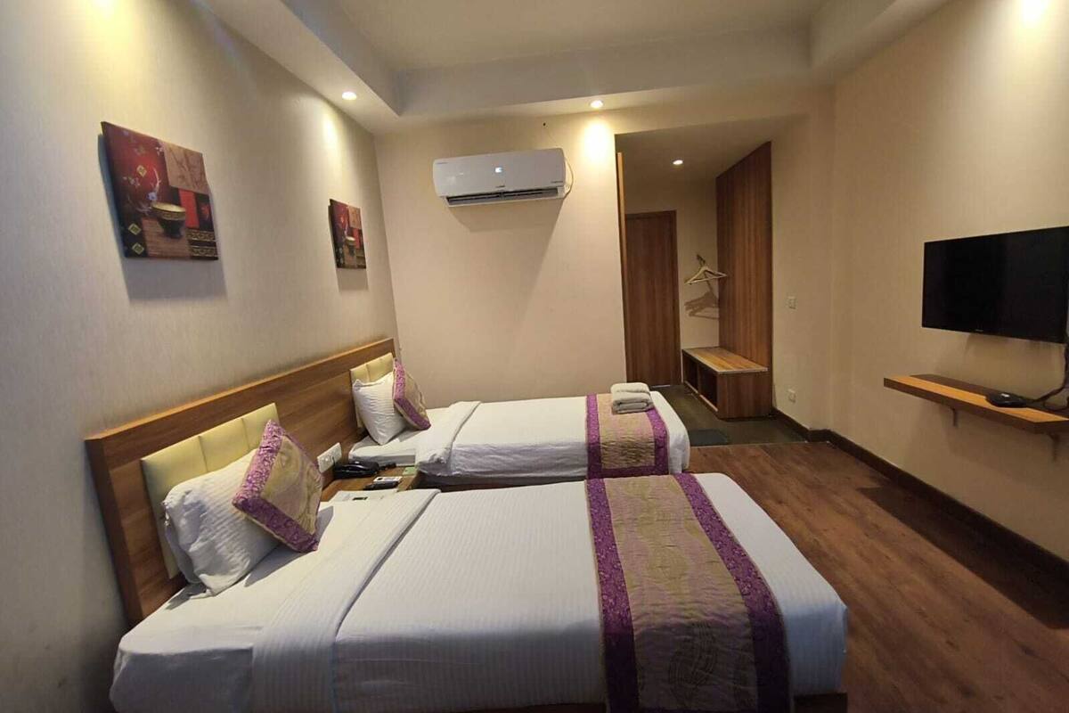 A hotel room with two beds, a TV, an air conditioner, and a wooden floor.