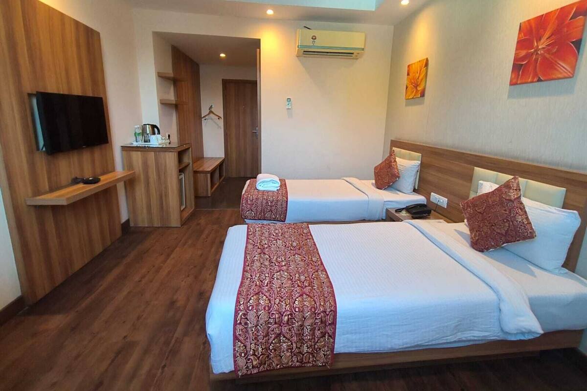 A hotel room with two beds, a TV, a desk, and an air conditioner.