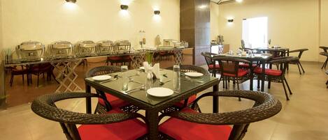 A dining area with multiple tables and chairs, buffet setup, and ceiling lights.