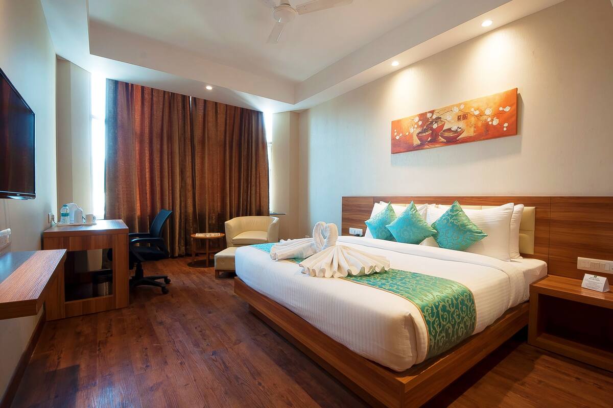 A hotel room with a large bed, a desk, a chair, and a painting on the wall.