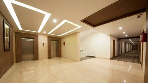 A spacious, well-lit hallway with marble flooring, wooden paneling, and a long corridor leading to a door. - Hotel Le Roi Haridwar @ Har Ki Pauri Road (Haridwar)