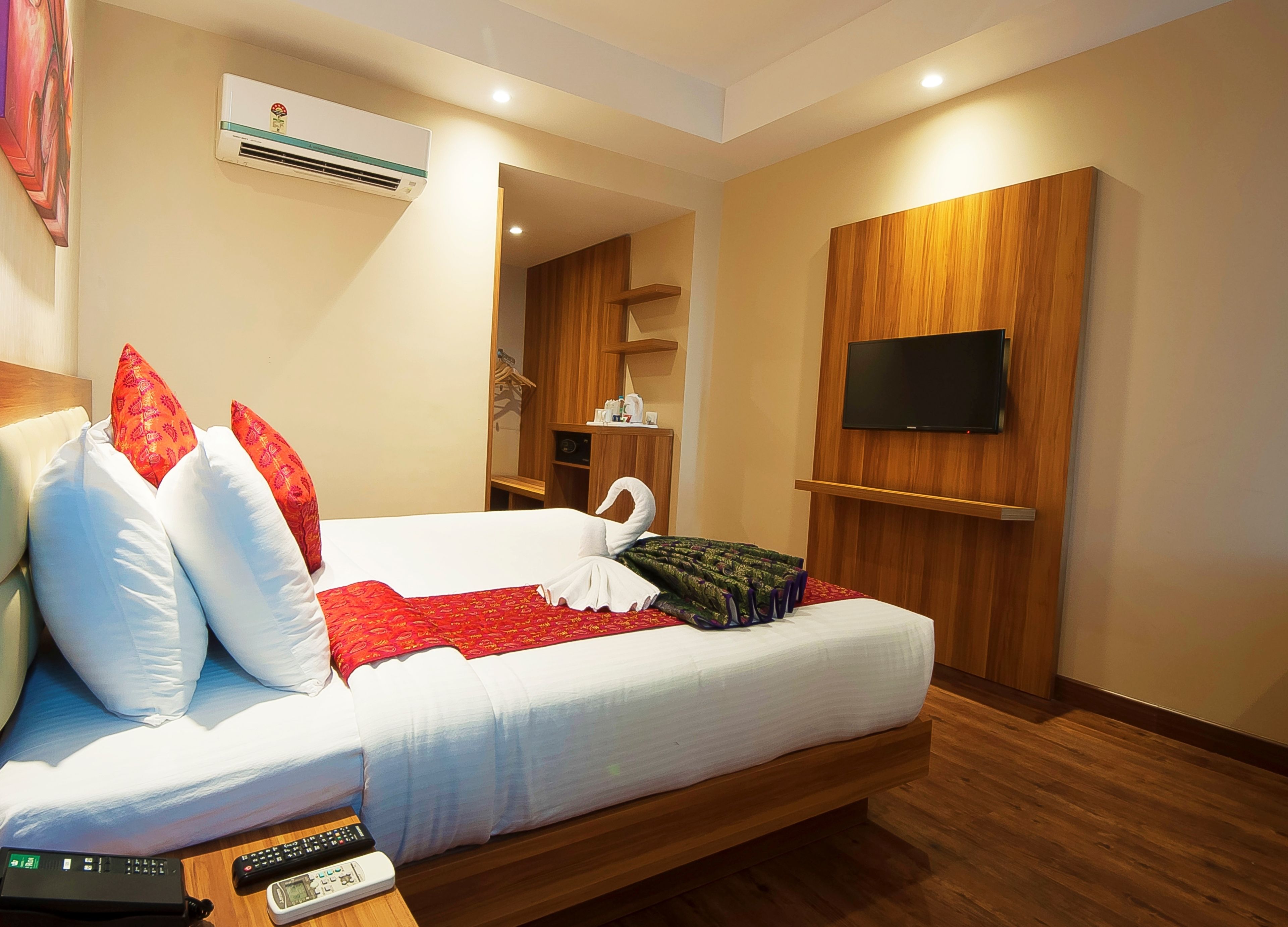 A hotel room with a bed, pillows, a TV, a remote control, and an air conditioning unit.