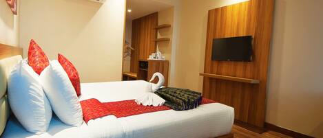 A hotel room with a bed, pillows, a TV, a remote control, and an air conditioning unit.