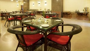 A spacious restaurant with multiple tables and chairs, featuring a modern design with glass tops and wicker chairs. - Hotel Le Roi Haridwar @ Har Ki Pauri Road (Haridwar)