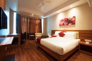 Une chambre d’hôtel avec un lit en bois, un bureau, une chaise, une télévision et un tableau au mur.