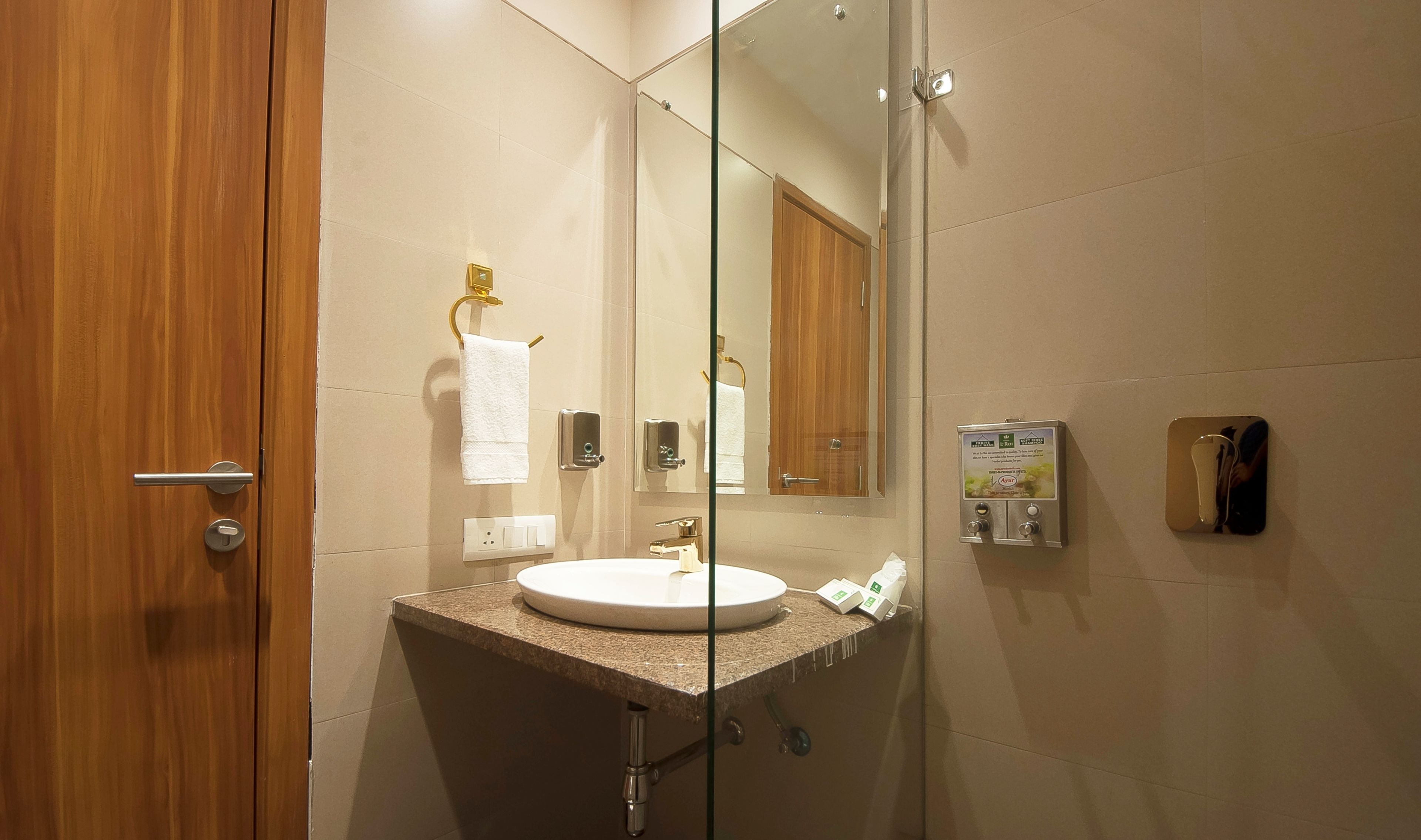 A bathroom with a wooden door, a white sink, a mirror, and a towel rack.