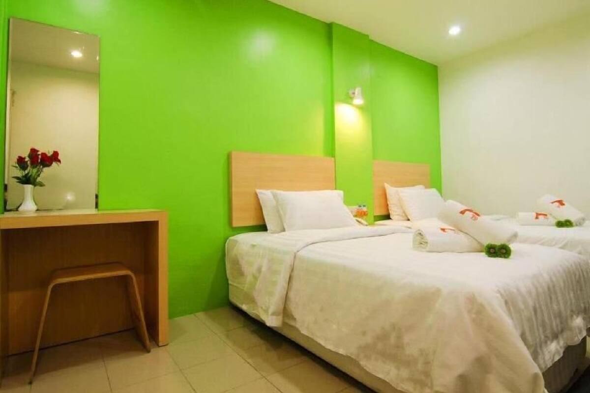 A hotel room with two beds, a desk, a chair, a mirror, and a vase with flowers.