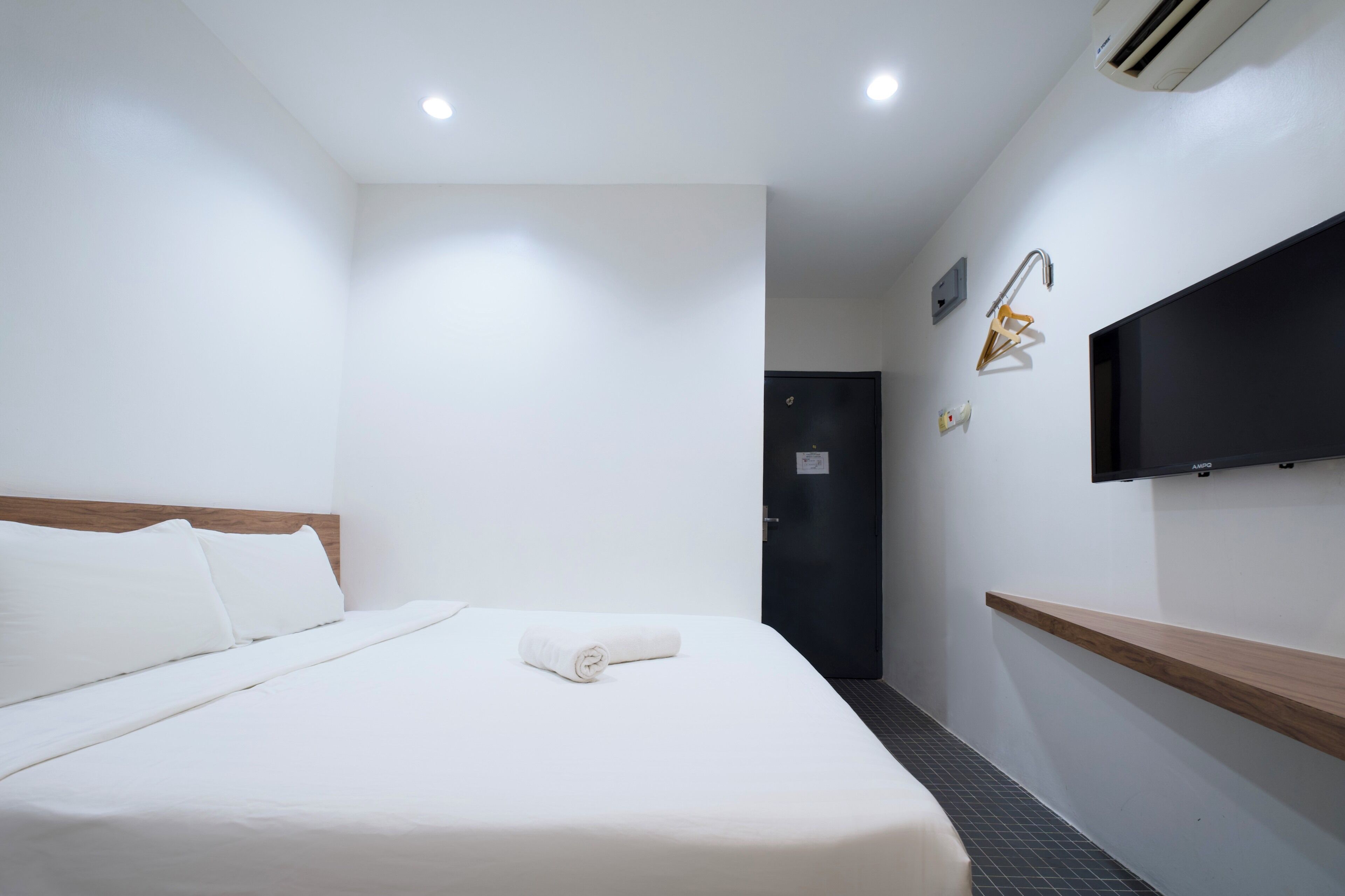 Habitación de hotel con una cama, un televisor de pantalla plana en la pared, un estante de madera y una puerta.