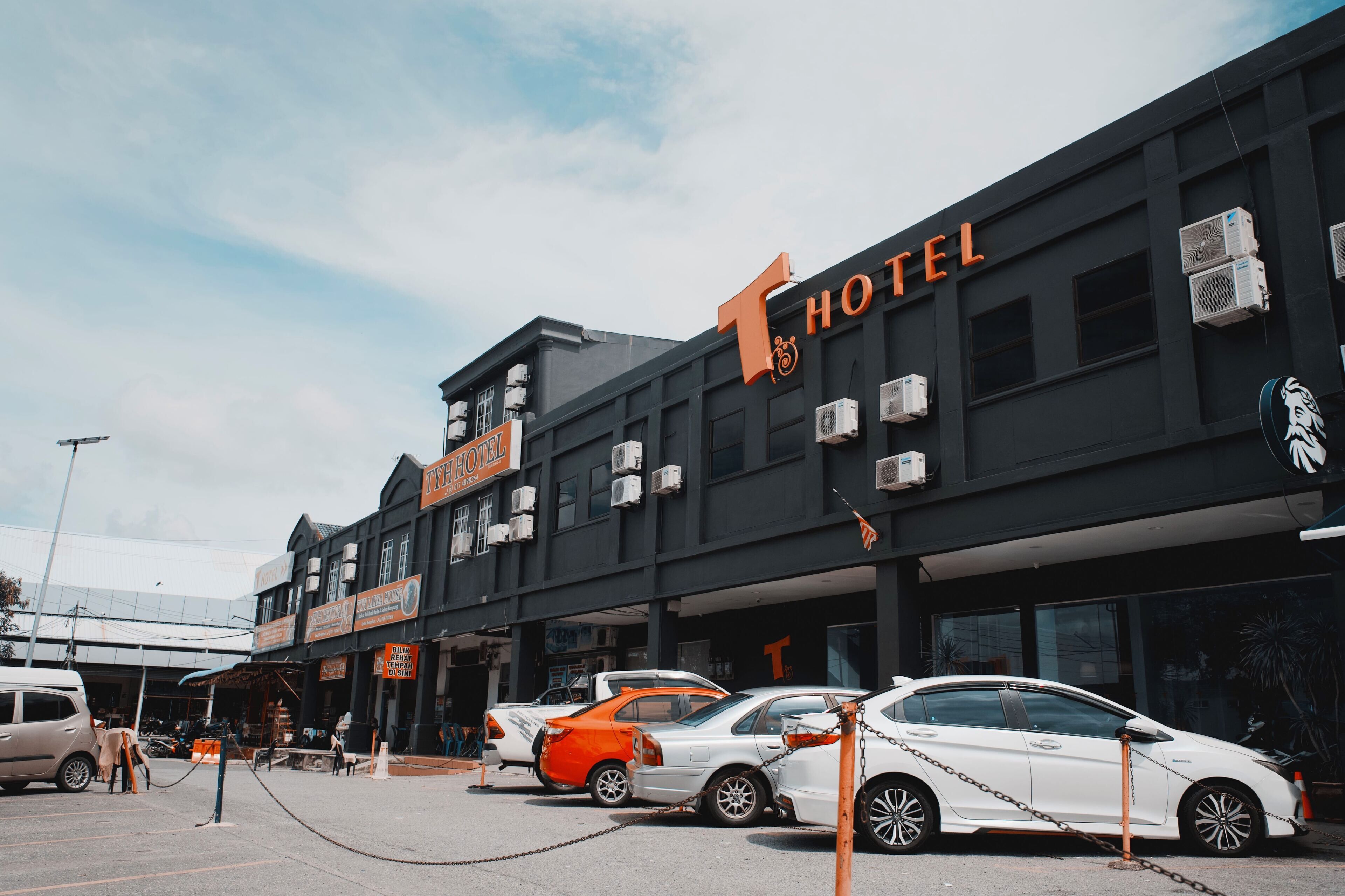 Een hotel met een opvallend 'HOTEL'-bord, meerdere airconditioners en geparkeerde auto's ervoor.