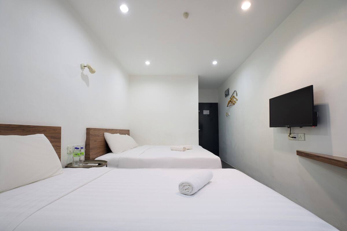 A hotel room with two beds, a TV mounted on the wall, and a small table with a bottle and glasses.