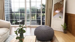 A living room with a large window, a sofa, a round ottoman, a mirror, and a staircase.