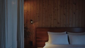 A wooden-paneled room with a bed, a nightstand, and a wall-mounted light.