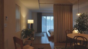 A hotel room with a bed, a desk, a chair, a lamp, and a potted plant.