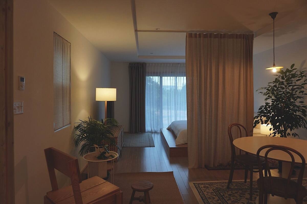 A hotel room with a bed, a desk, a chair, a lamp, and a potted plant.