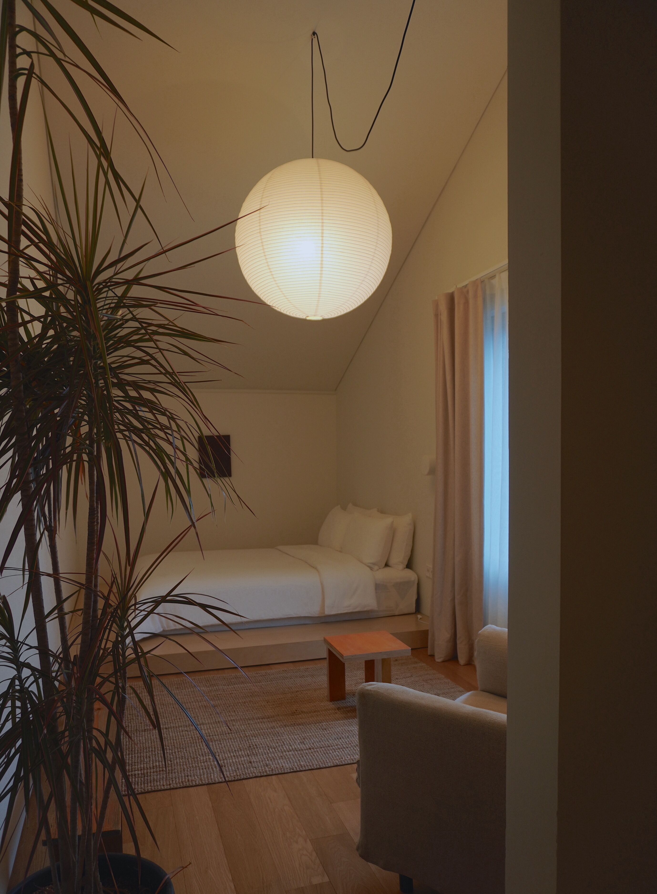Un dormitorio acogedor con cama, mesita de noche, una silla, lámpara colgante y una planta en maceta.