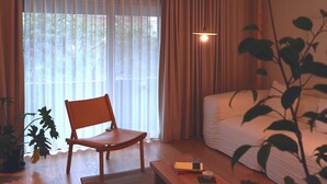 A room with a wooden chair, a sofa, a coffee table, and a large window with curtains.