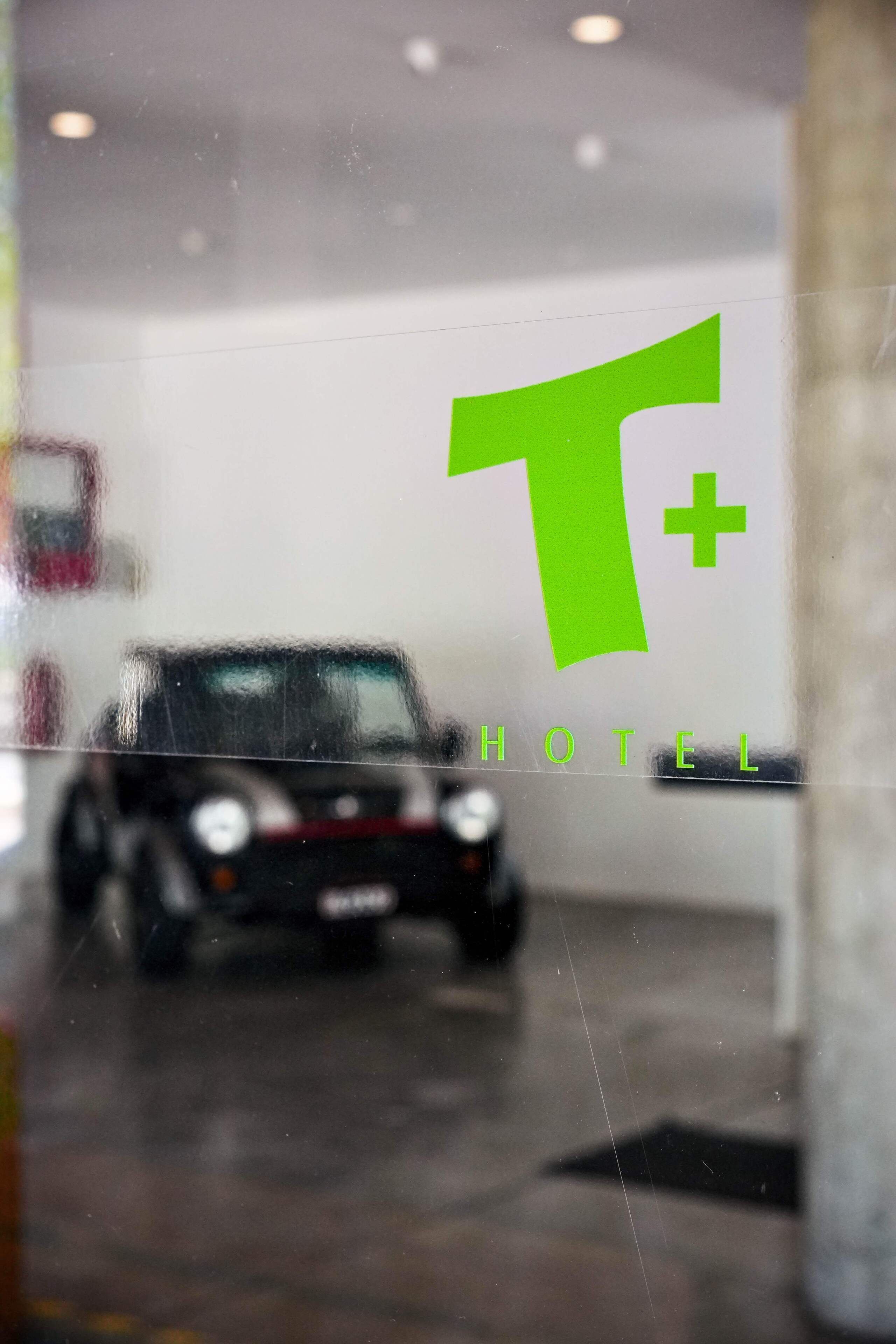 A car inside a building with a large green 'T+' logo and the word 'HOTEL' visible on the wall.