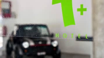 A car inside a building with a large green 'T+' logo and the word 'HOTEL' visible on the wall.