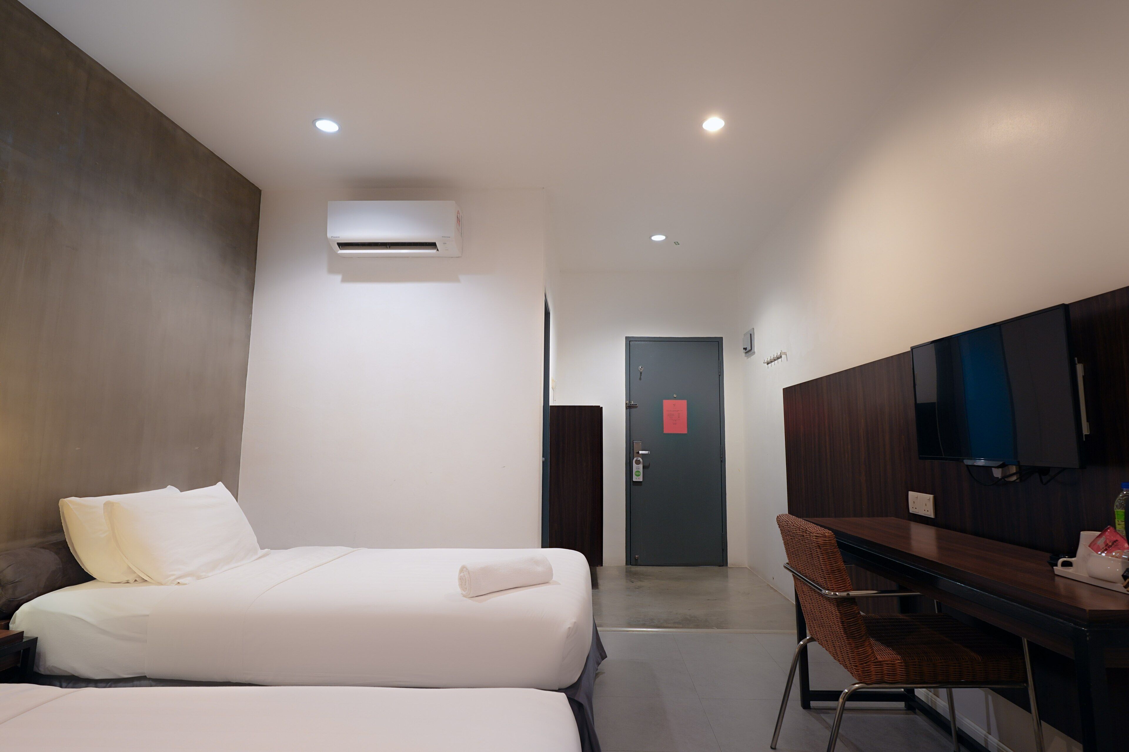 A hotel room with two beds, a desk, a chair, a TV, and an air conditioning unit.