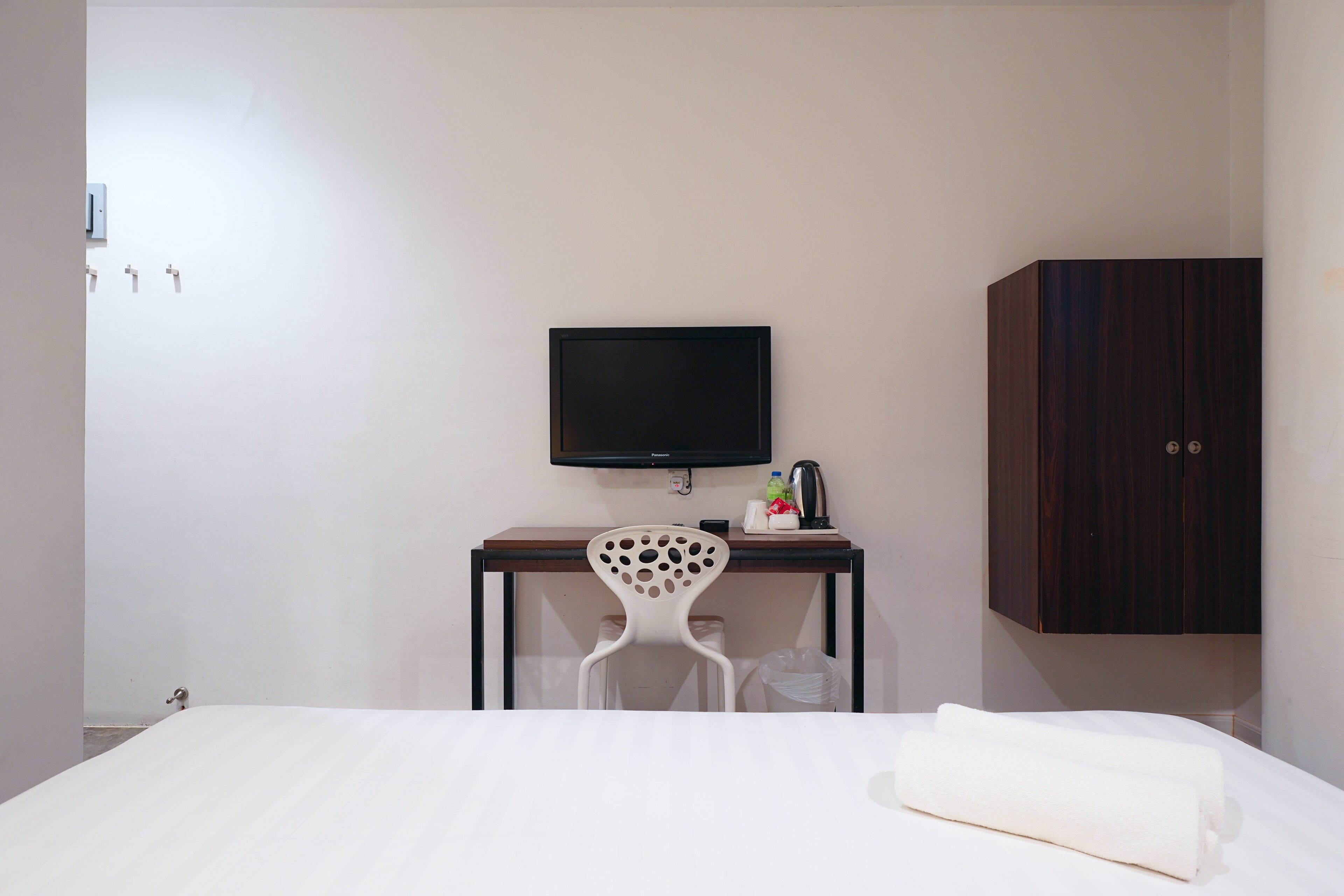 A hotel room with a bed, a desk with a TV, a chair, and a wardrobe.